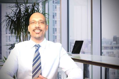 Smiling man in a white shirt and striped tie in an office with a laptop and plants in the background