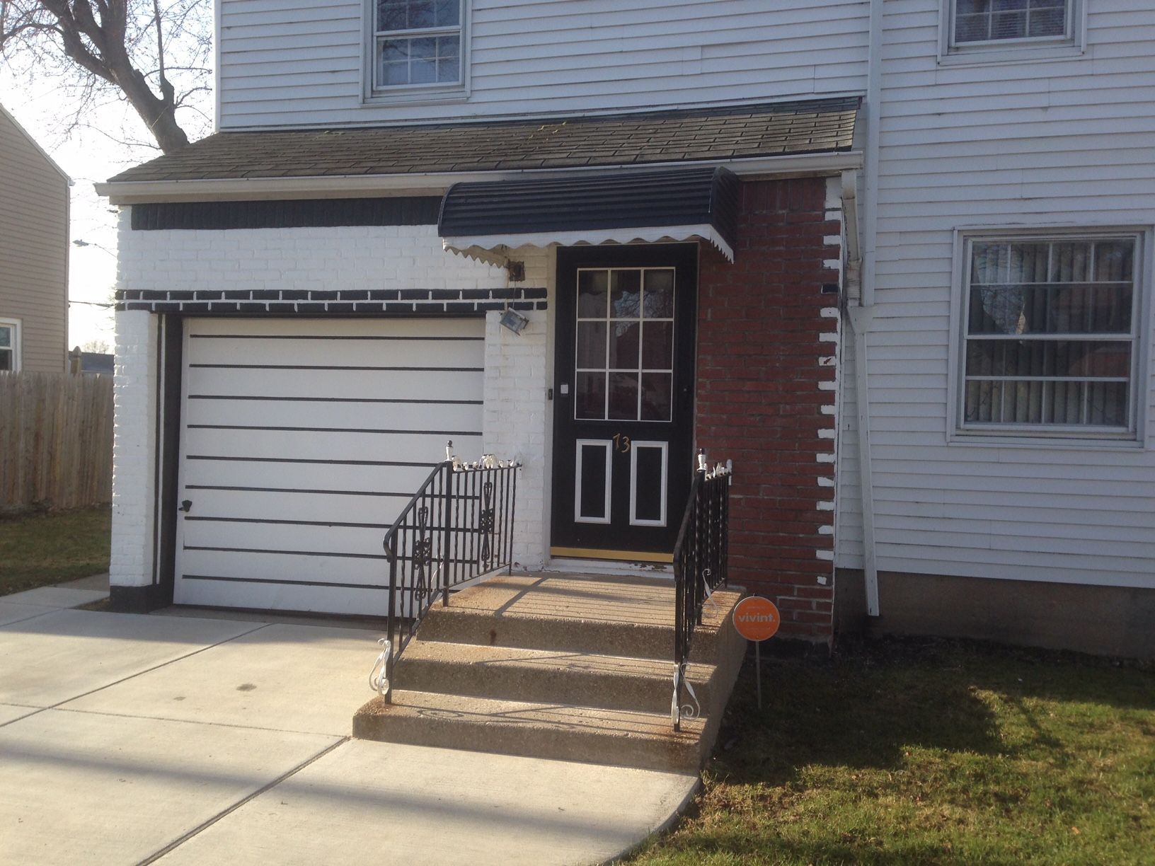 Two-story white house with attached garage, red brick accent, and steps leading to a front door with a small awning.