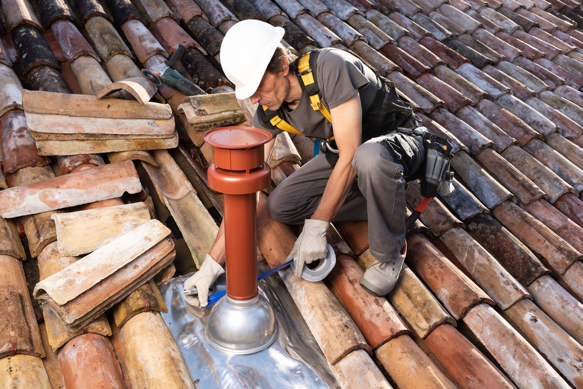 Roofer sealing a roof vent while performing repairs on a clay tile roof. Roofer sealing a roof vent while performing repairs on a clay tile roof.