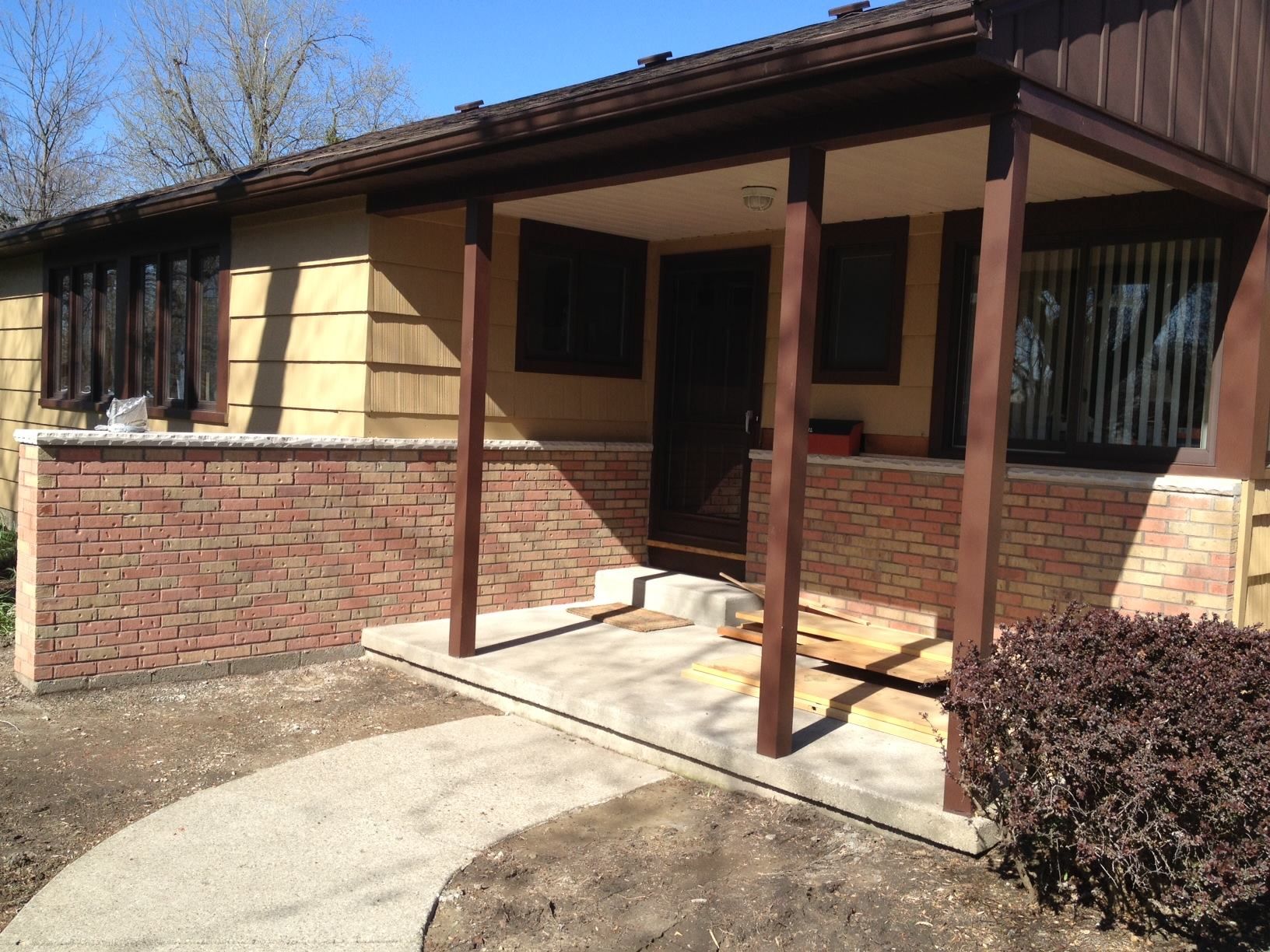 Brown and yellow house with brick accents, covered porch, and concrete walkway.
