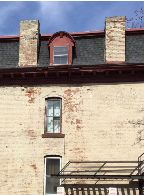 Old brick building facade with red dormer windows and a metal awning against a blue sky
