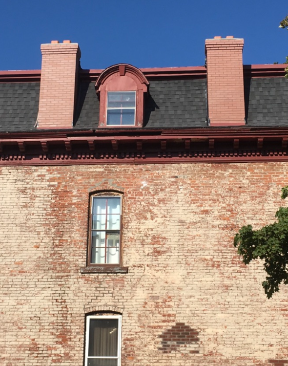 Brick building facade with dormer windows and red trim against a clear blue sky