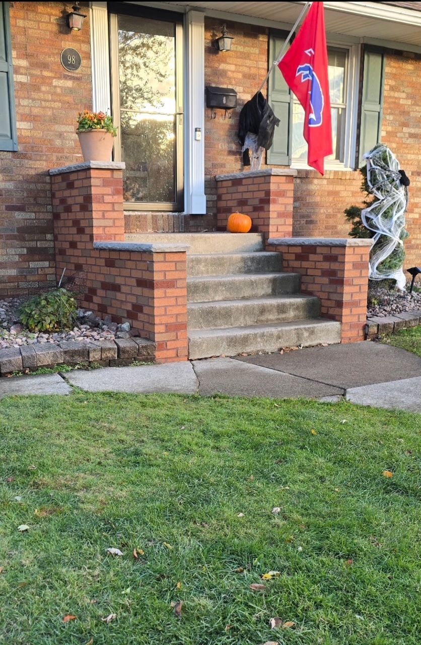 Front porch with brick steps, pumpkin, red flag, and Halloween skeleton decoration by a brick house