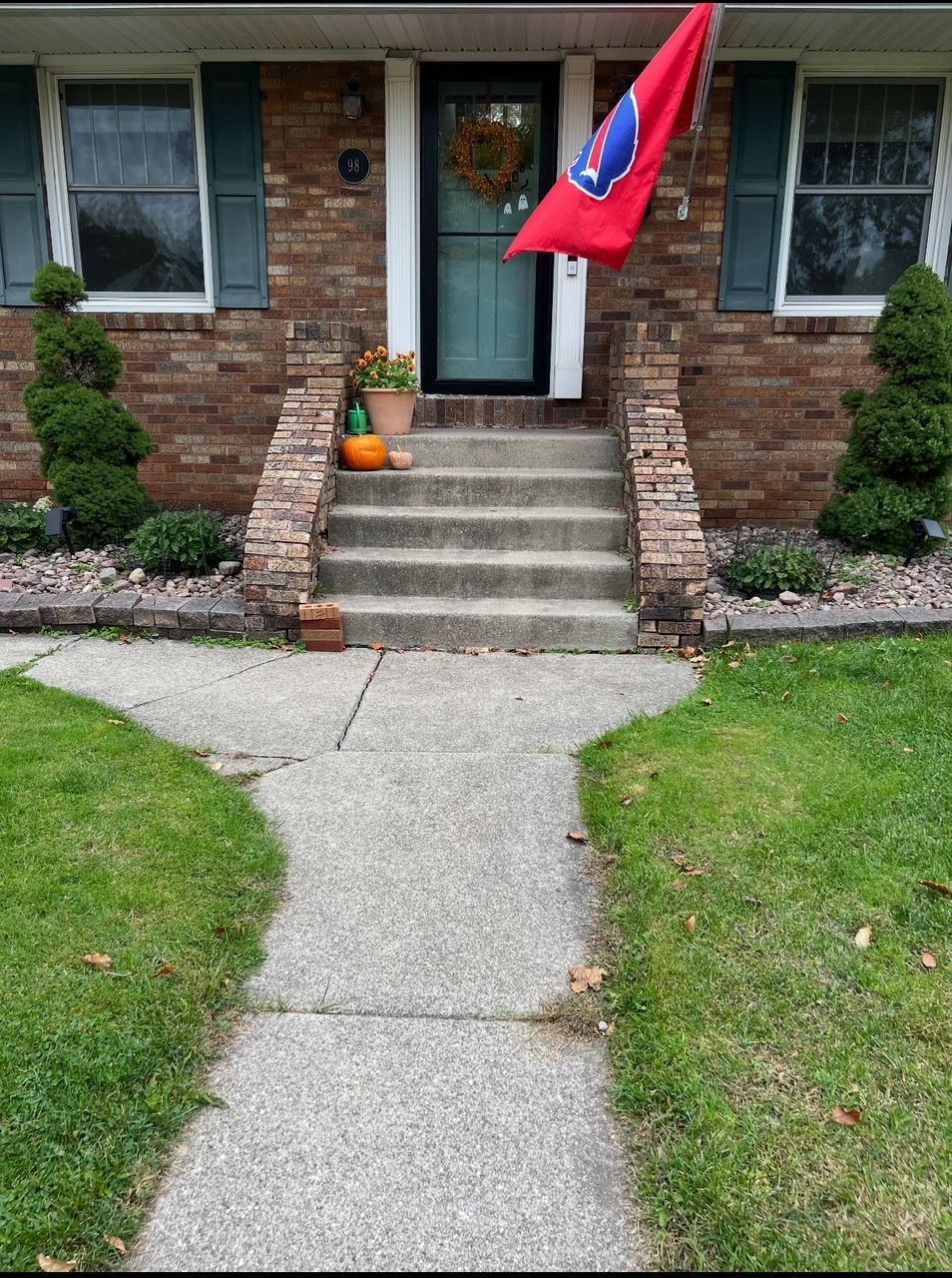 Brick house entry with steps, cracked sidewalk, and a red flag by the front door