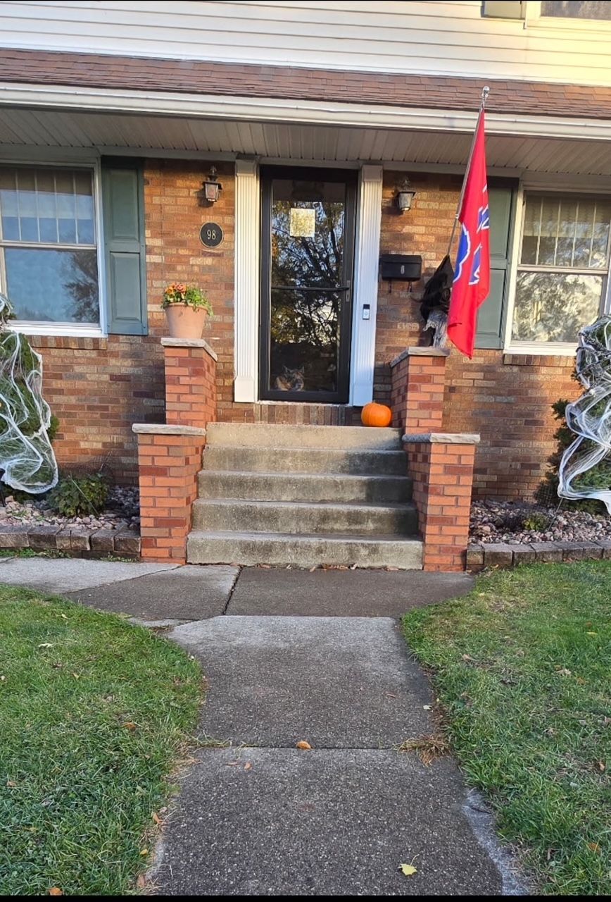 Brick house front porch with steps, concrete walkway, and a red flag by the door