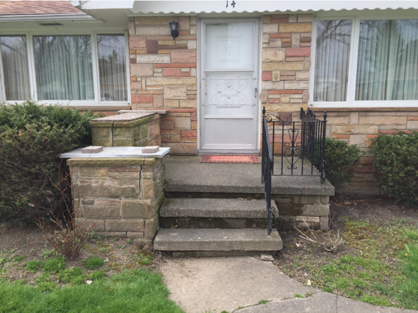Front entrance of a house with concrete steps, black handrail, stone planters, and a white storm door.