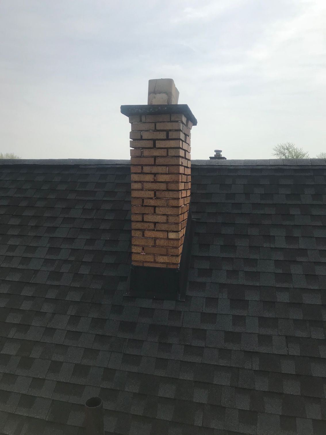Brick chimney on a dark shingled roof under a cloudy sky
