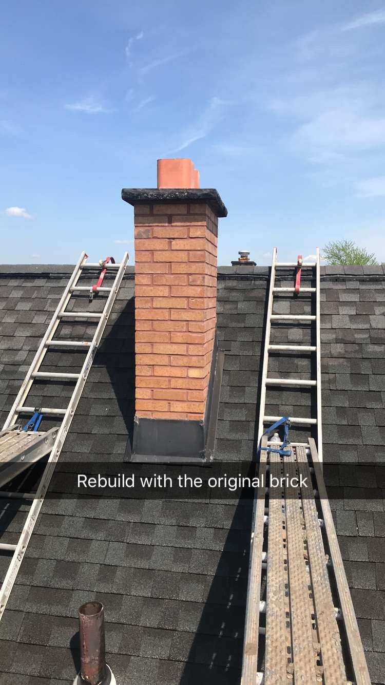 Roof with brick chimney under repair, flanked by two ladders and a darker surrounding shingle roof.
