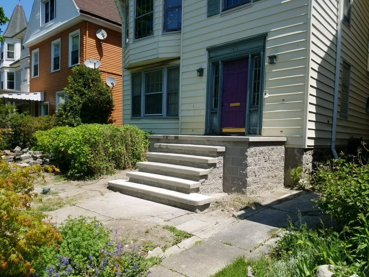 Front steps to a gray house with a purple door and small garden