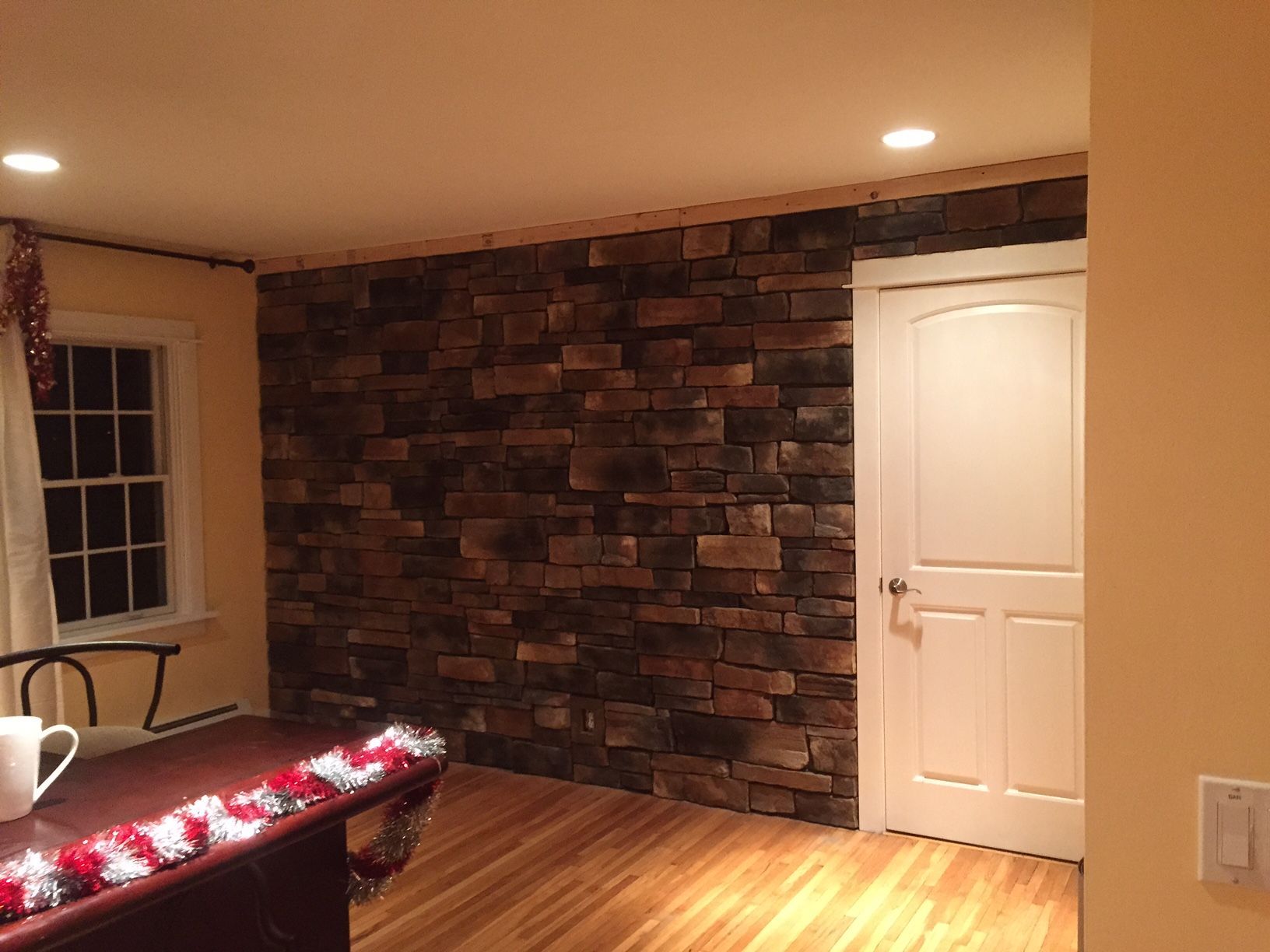 Interior room with stone accent wall and white door. Wooden floor and tan walls.