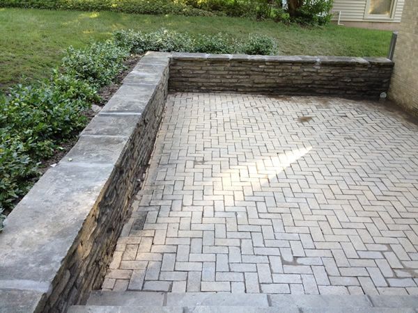 Stone patio with low retaining walls and herringbone brick pattern.