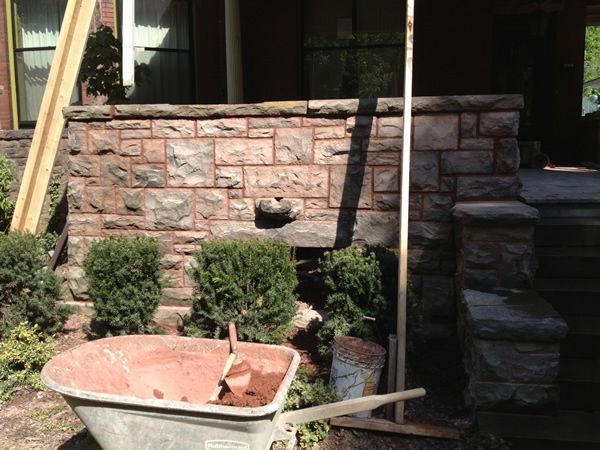 Stone wall construction with wheelbarrow of mortar, bushes, and steps.