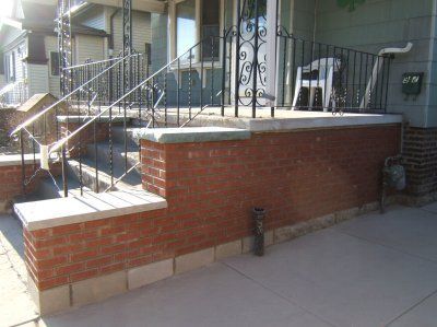 Brick porch steps with black railing, light-colored caps, and a small porch with a white chair.
