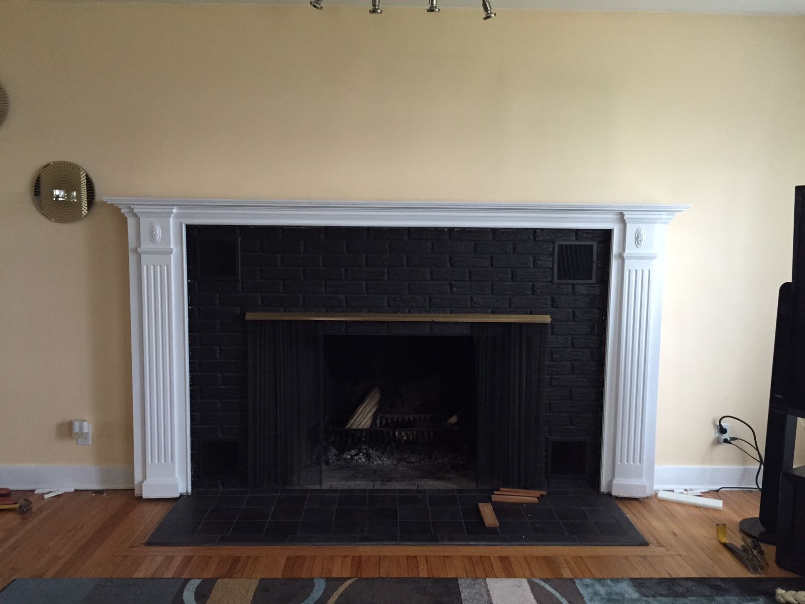 Fireplace with white mantle, black brick, and dark hearth on a yellow wall.