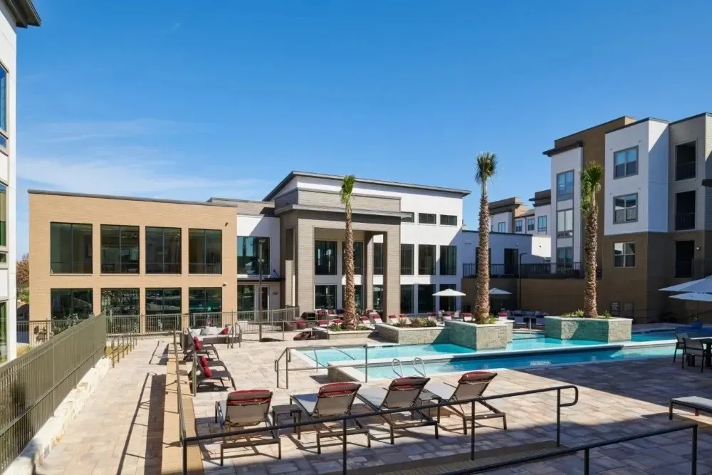 Outdoor community pool area with lounge chairs and palm trees