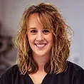 Smiling woman with curly light brown hair against a gray background.