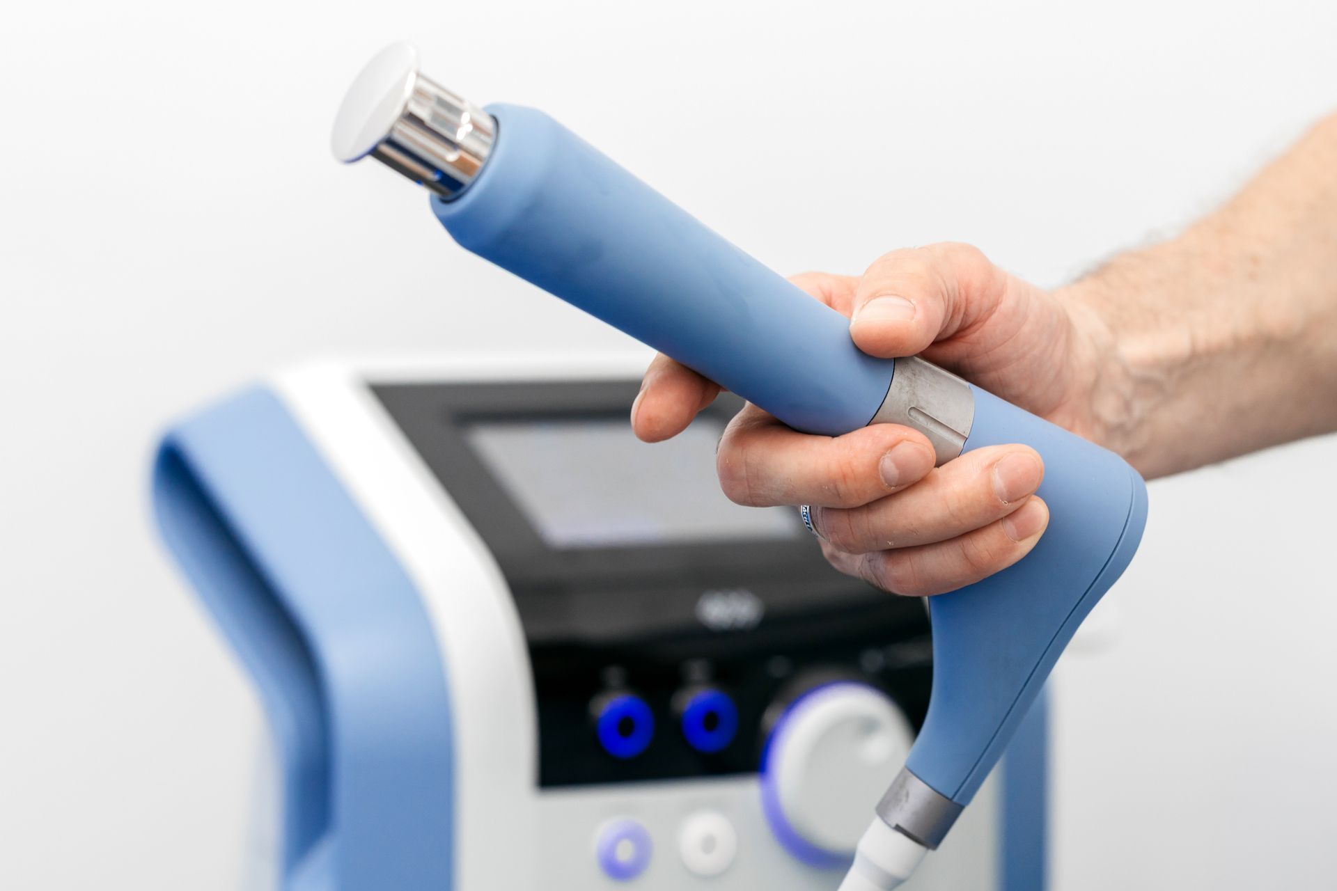 Hand holding a blue medical device wand beside a clinical machine interface.