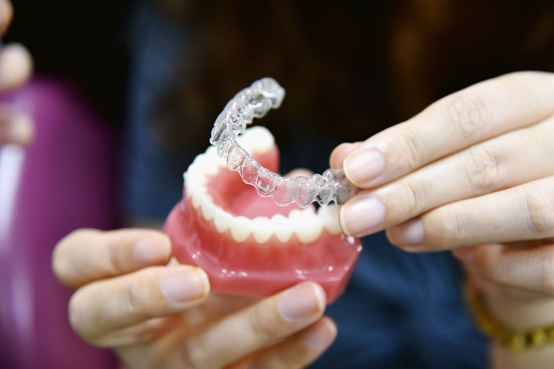 Hands holding clear dental aligner over a pink model of teeth.