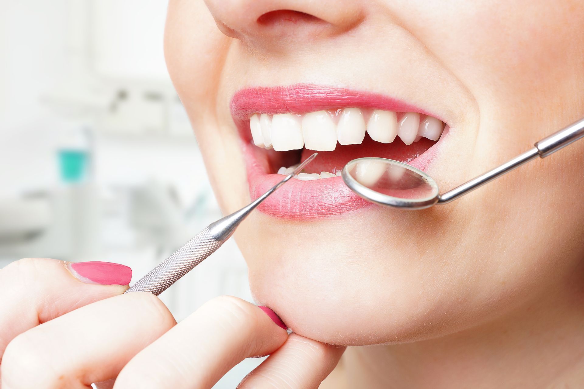 Dentist examining teeth with a mouth mirror and dental tool, close-up of smiling mouth.