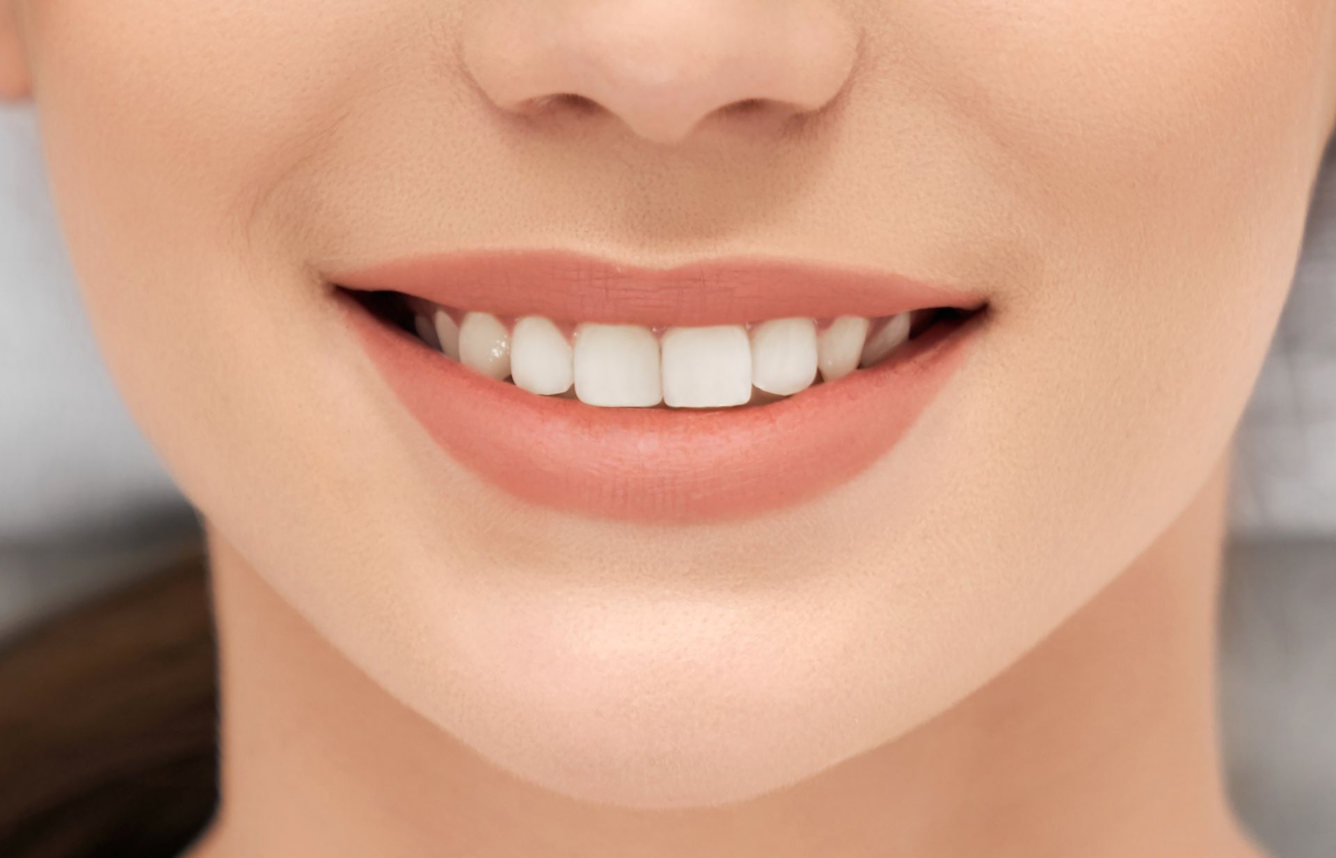 Close-up of a smiling mouth with white teeth and soft pink lips.