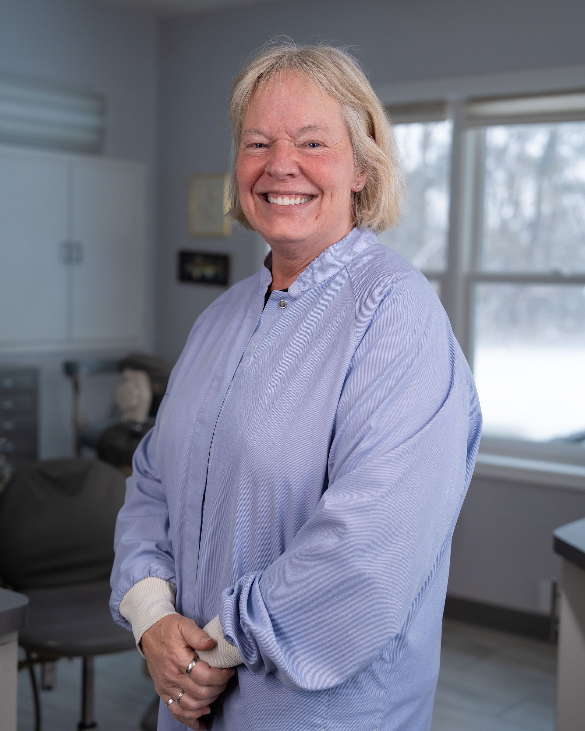 Smiling person in a light blue shirt standing in a bright kitchen or office setting.