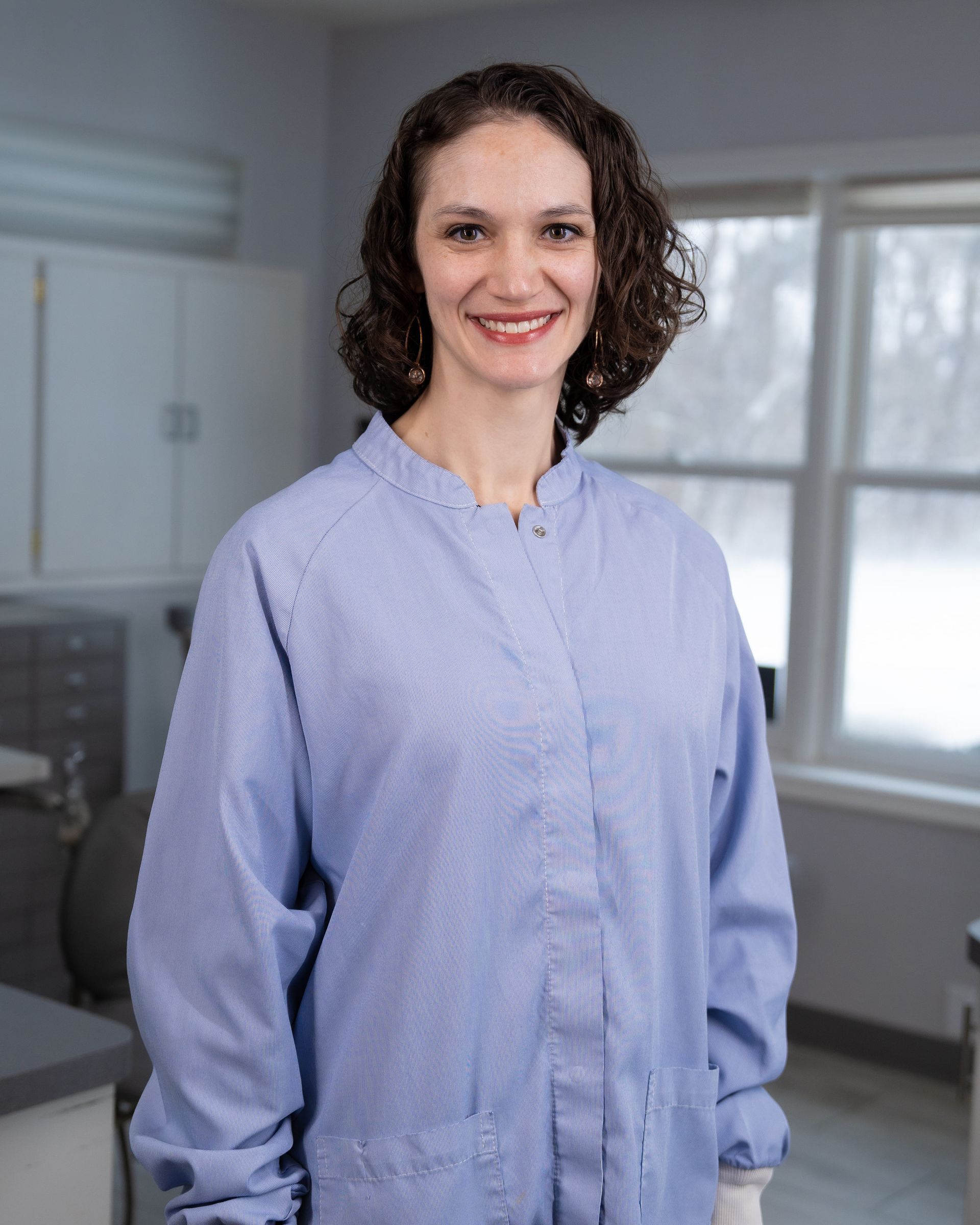 Smiling person in a light blue shirt standing in a bright office.