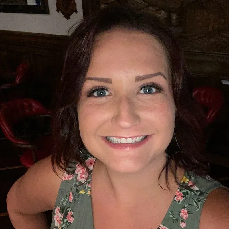 Smiling woman in a floral top, taking a selfie indoors.