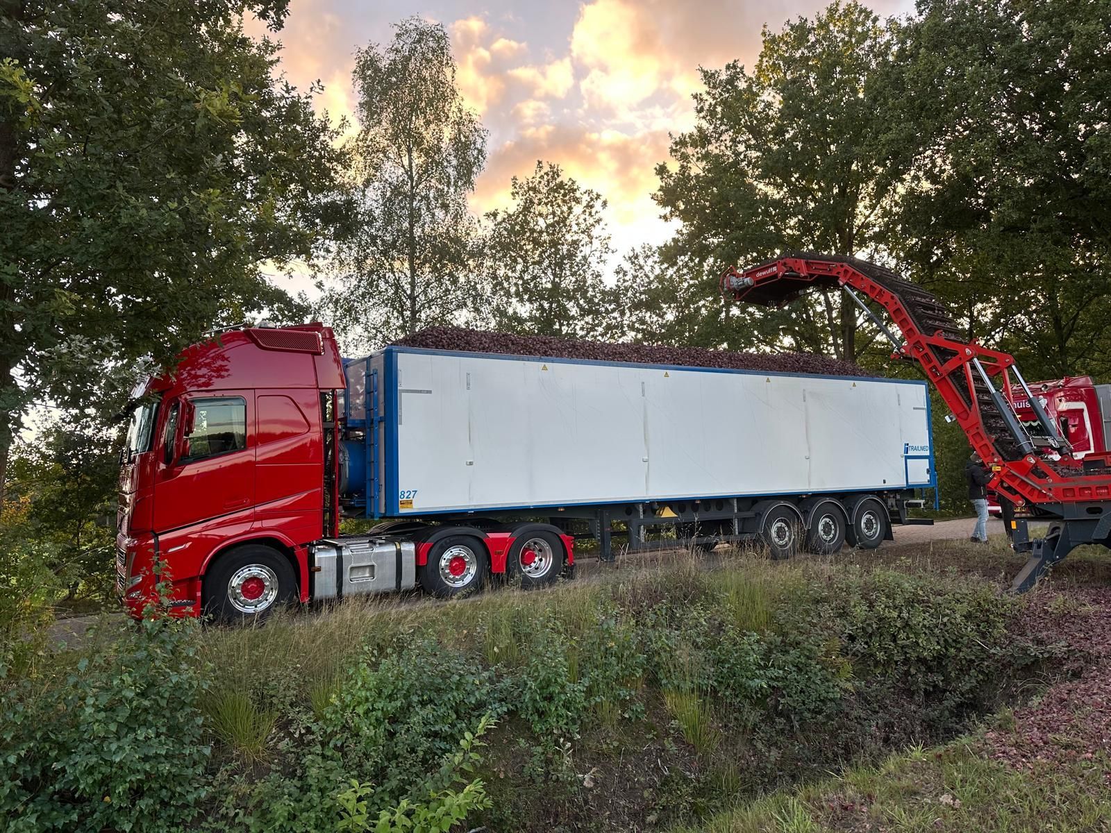 gebr-karsten-transport rode vrachtwagen wordt geladen door kraan in bosrijke omgeving