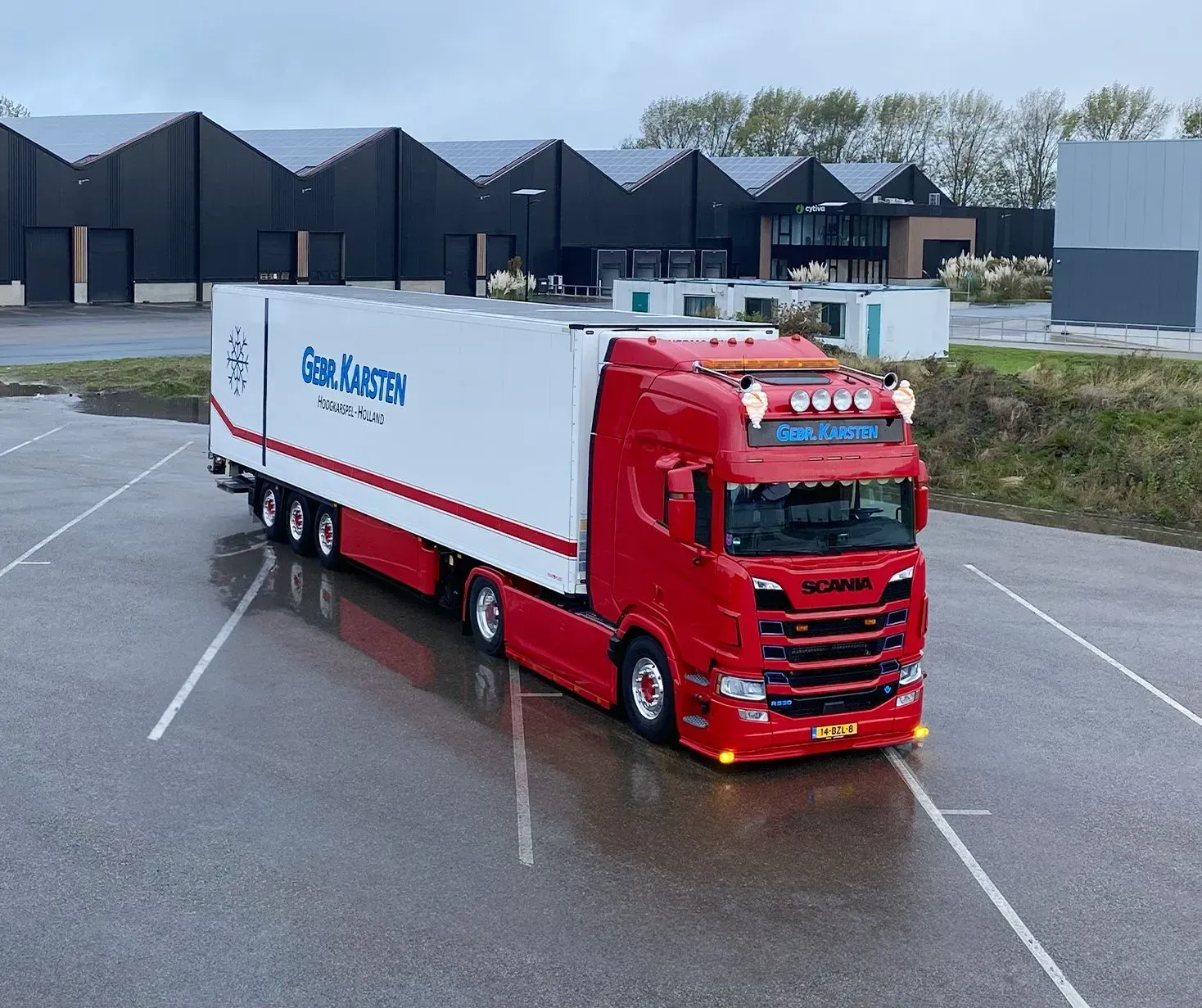 Rode Scania-vrachtwagen met witte oplegger op een parkeerplaats. Op de oplegger staat 