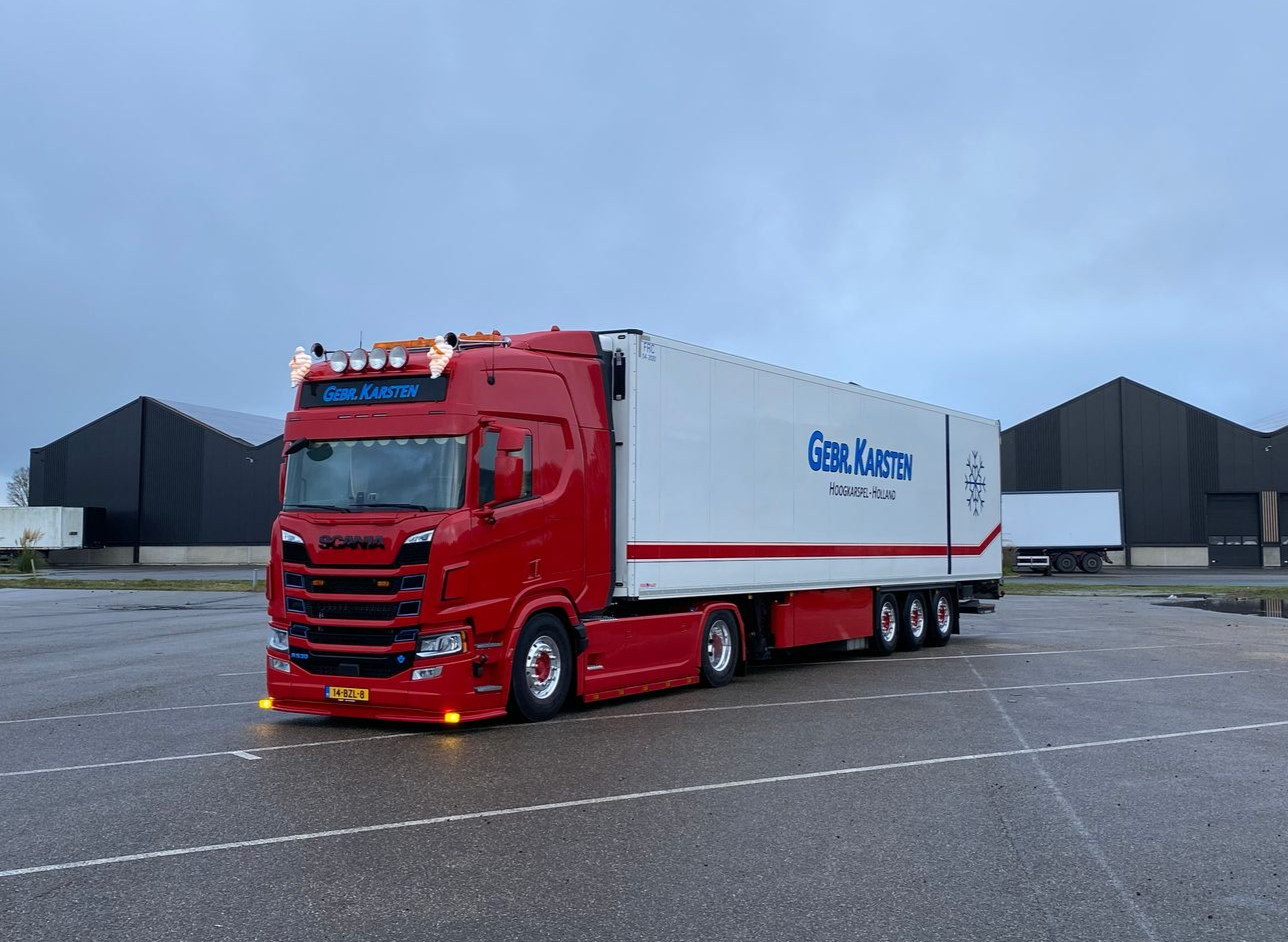 Rood-witte vrachtwagen met aanhanger, geparkeerd op een leeg terrein. 
