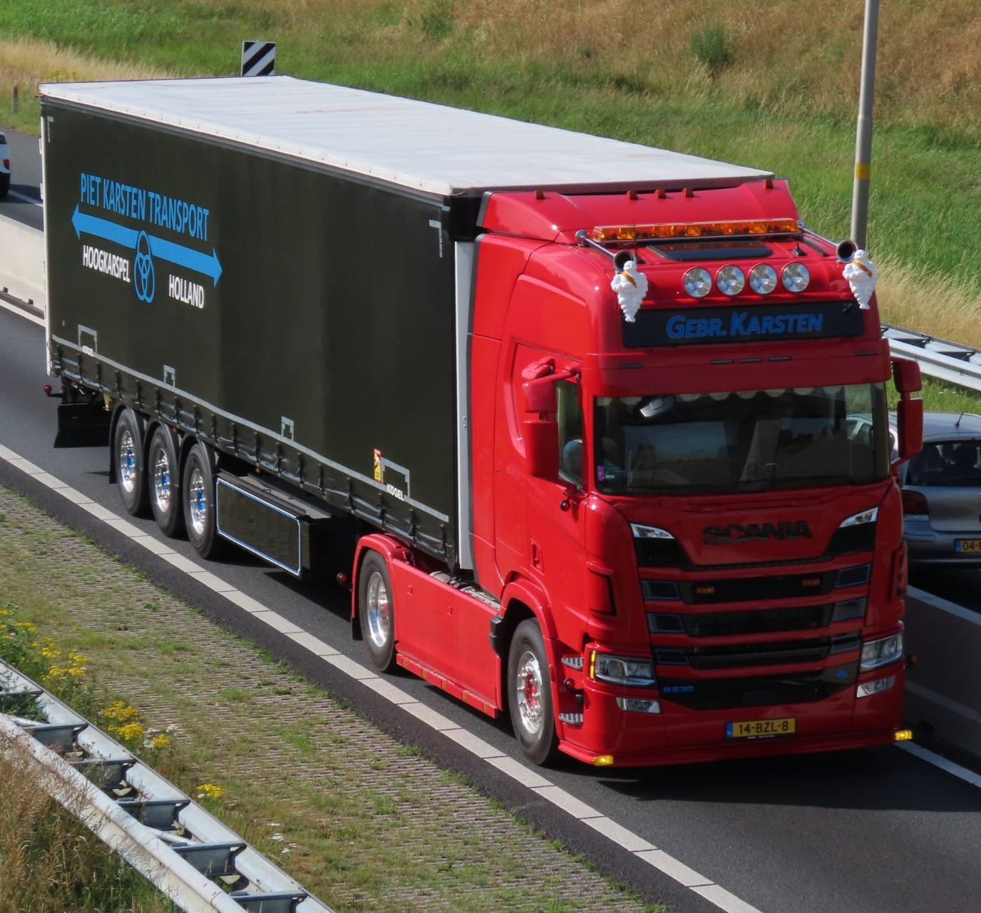 Rode Scania vrachtwagen op de snelweg, zwarte oplegger met de logo's 