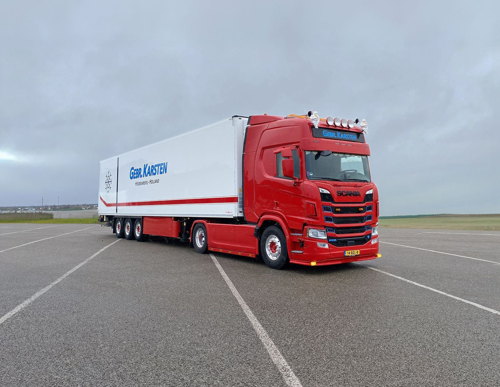 Rood-witte gebr-karsten-transport vrachtwagen op asfaltweg onder bewolkte lucht met Coldstore Express trailer.