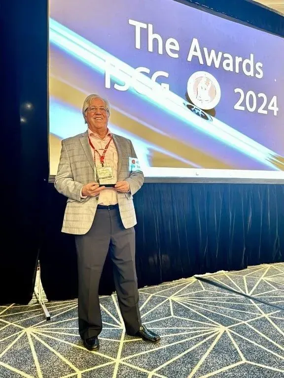 dr jason  in a blazer holds an award on a stage with a screen saying 