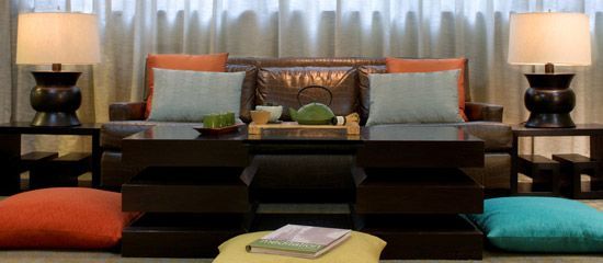 Hotel room with sofa, coffee table, lamps, and floor cushions.