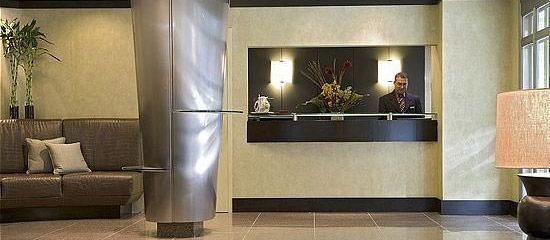 Hotel lobby with a receptionist, modern decor, brown sofa, metal pillar, and floor lamp.
