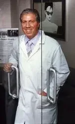 dr jason  in white coat smiles, holding glass door handles, with a portrait behind him.