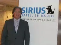 dr jason  in suit stands beside a Sirius Satellite Radio sign.