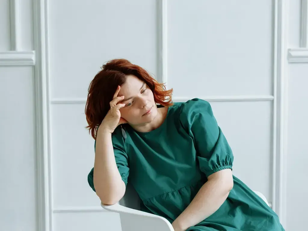 A woman experiencing burnout, sitting with her hand pressed to her head in exhaustion.