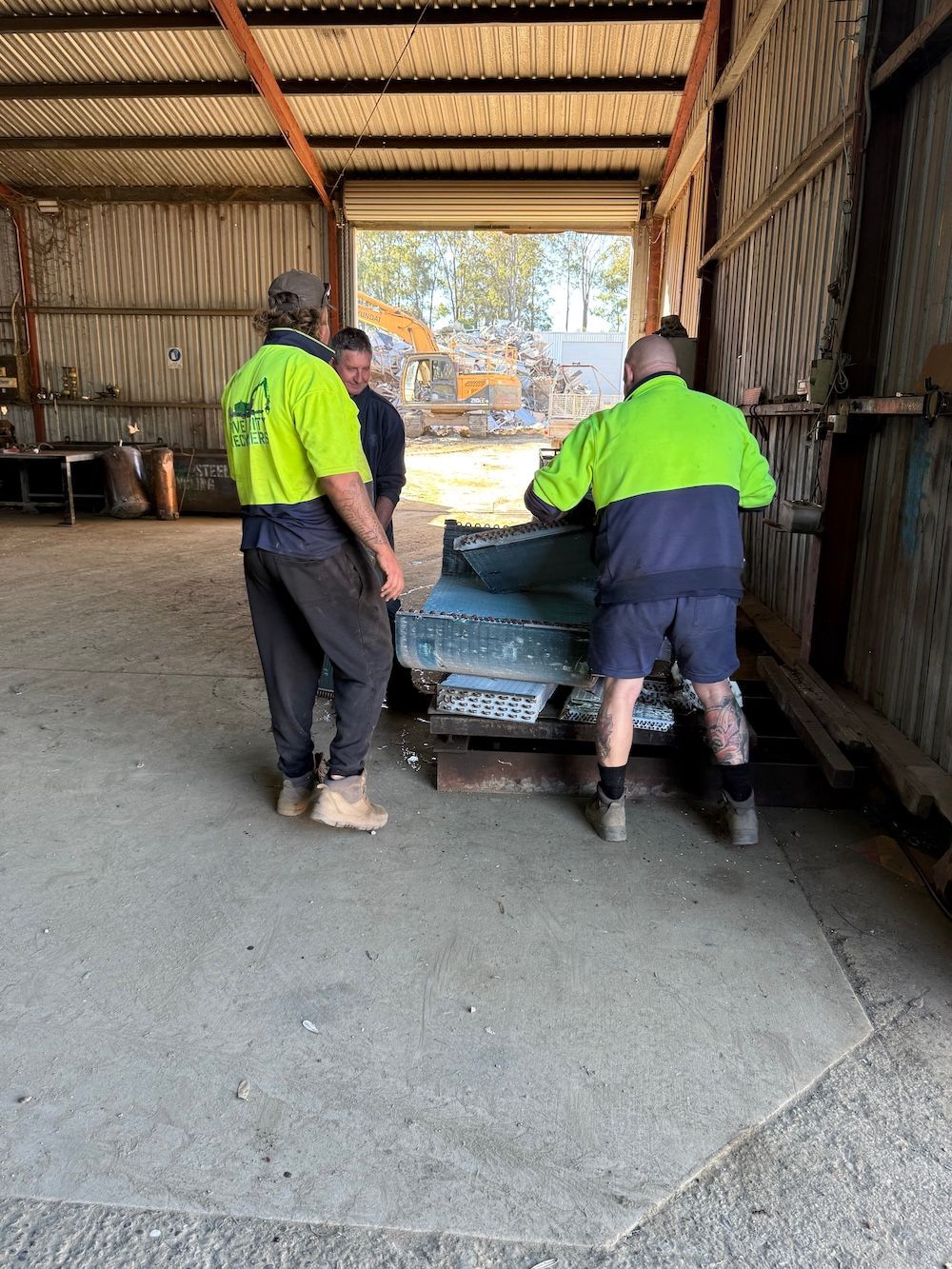 Two workers in neon jackets pushing a car inside a shed or garage.