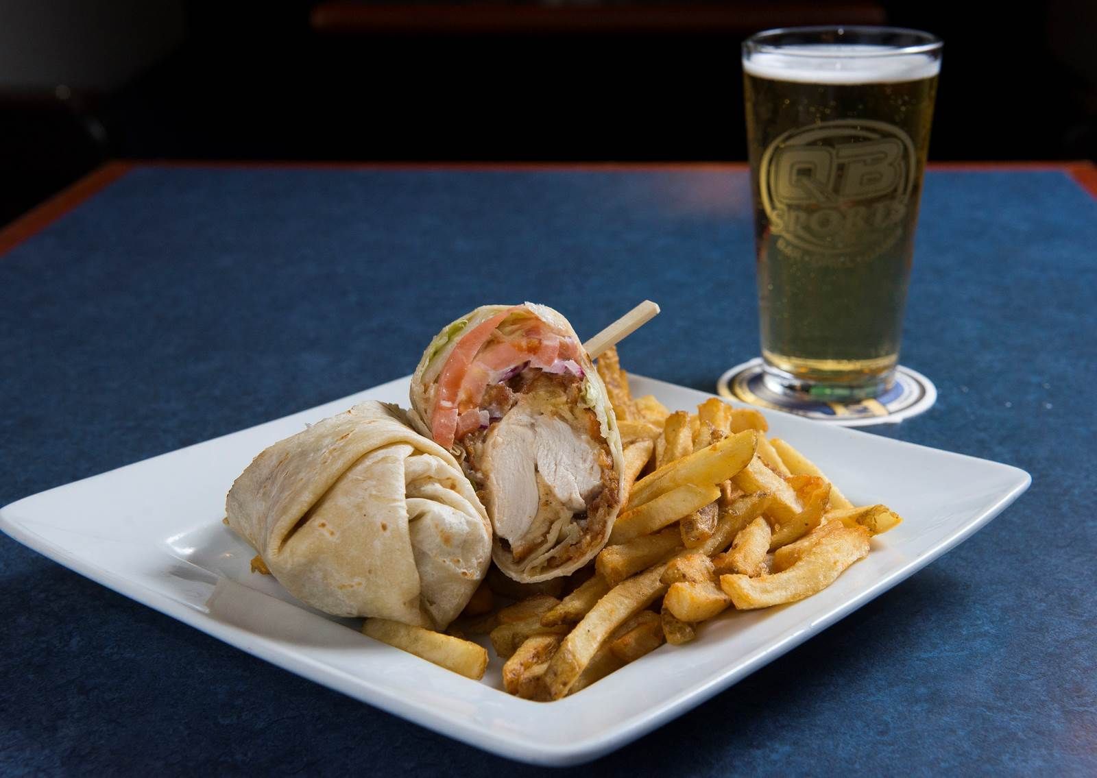 Sandwich with fries on a white plate beside a glass of beer on a table