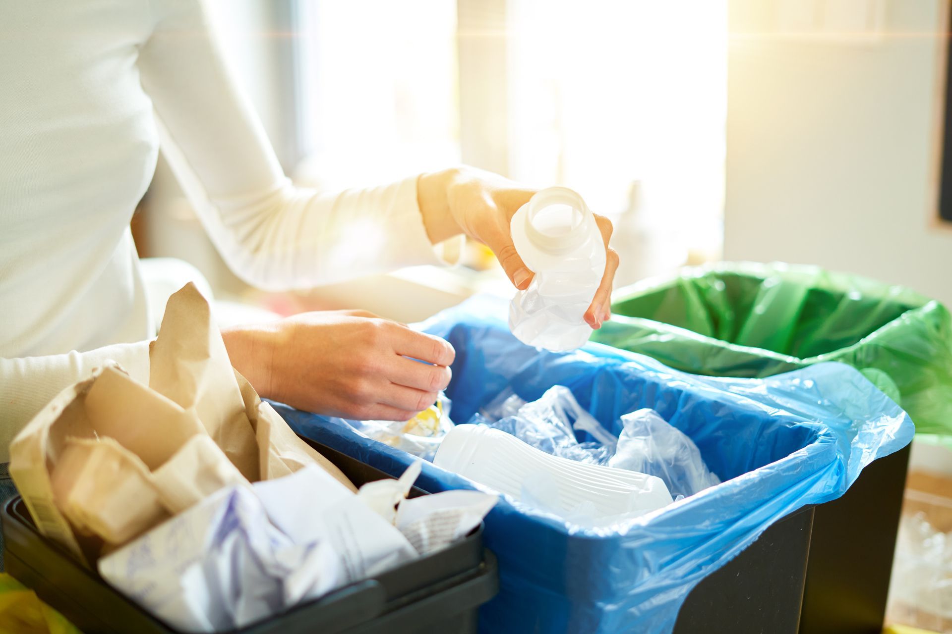 A woman is putting a plastic cup into a recycling bin.