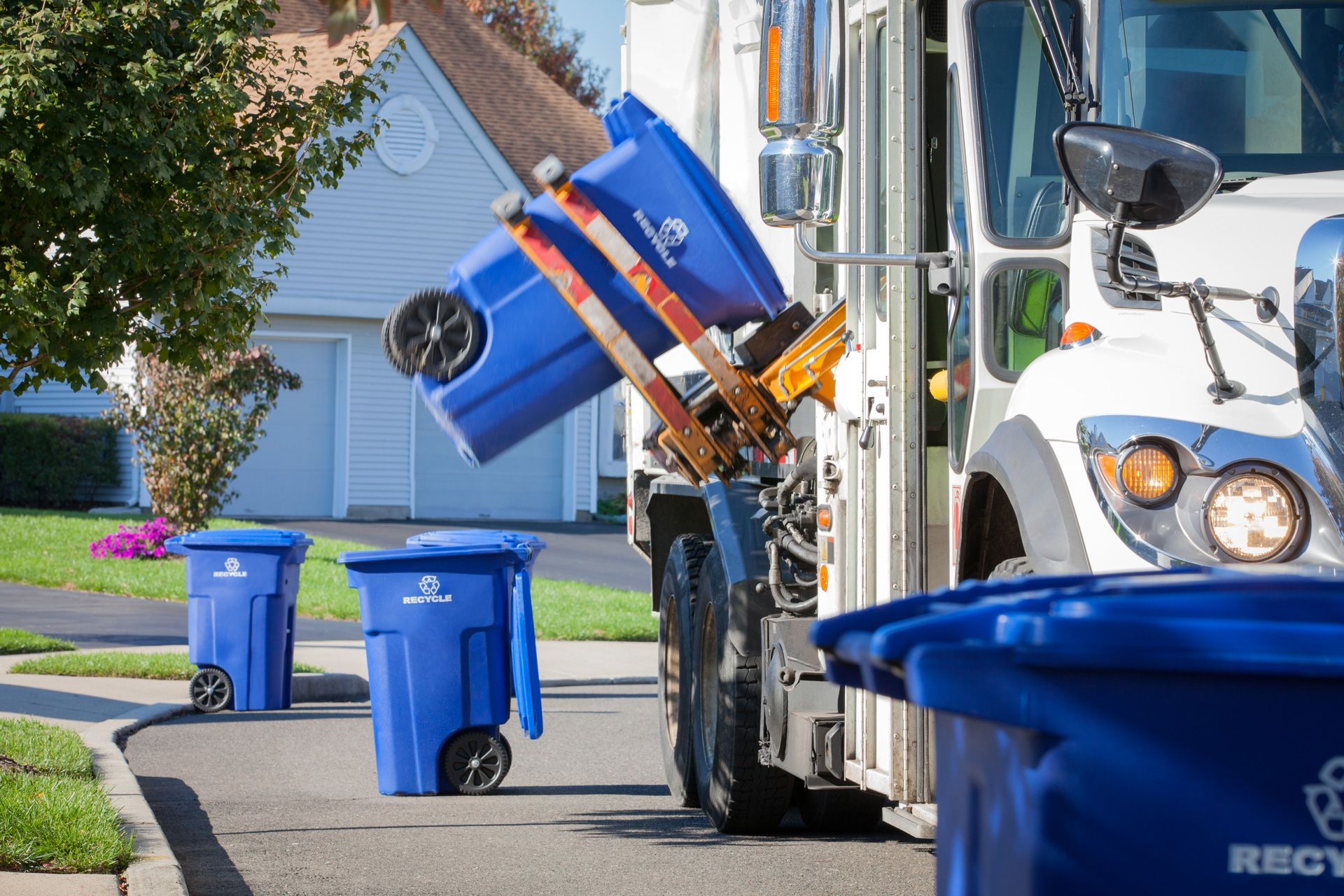 A blue trash can is being loaded into a recycling truck.