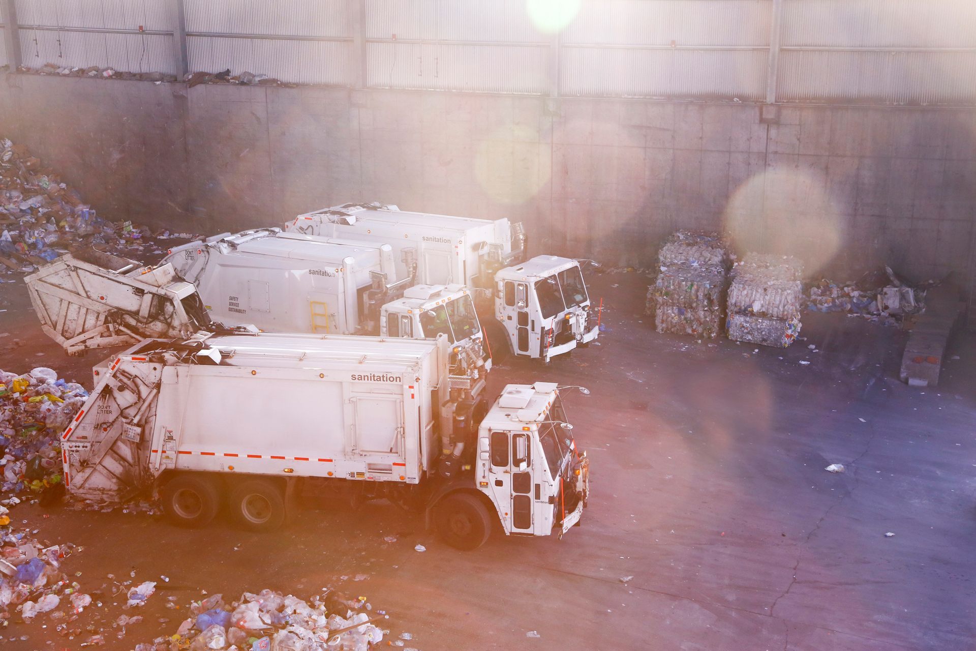 A garbage truck is driving through a pile of trash in a warehouse.