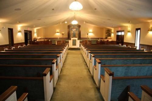 An interior view of a sanctuary featuring rows of pews facing a central altar and pulpit under warm lighting.