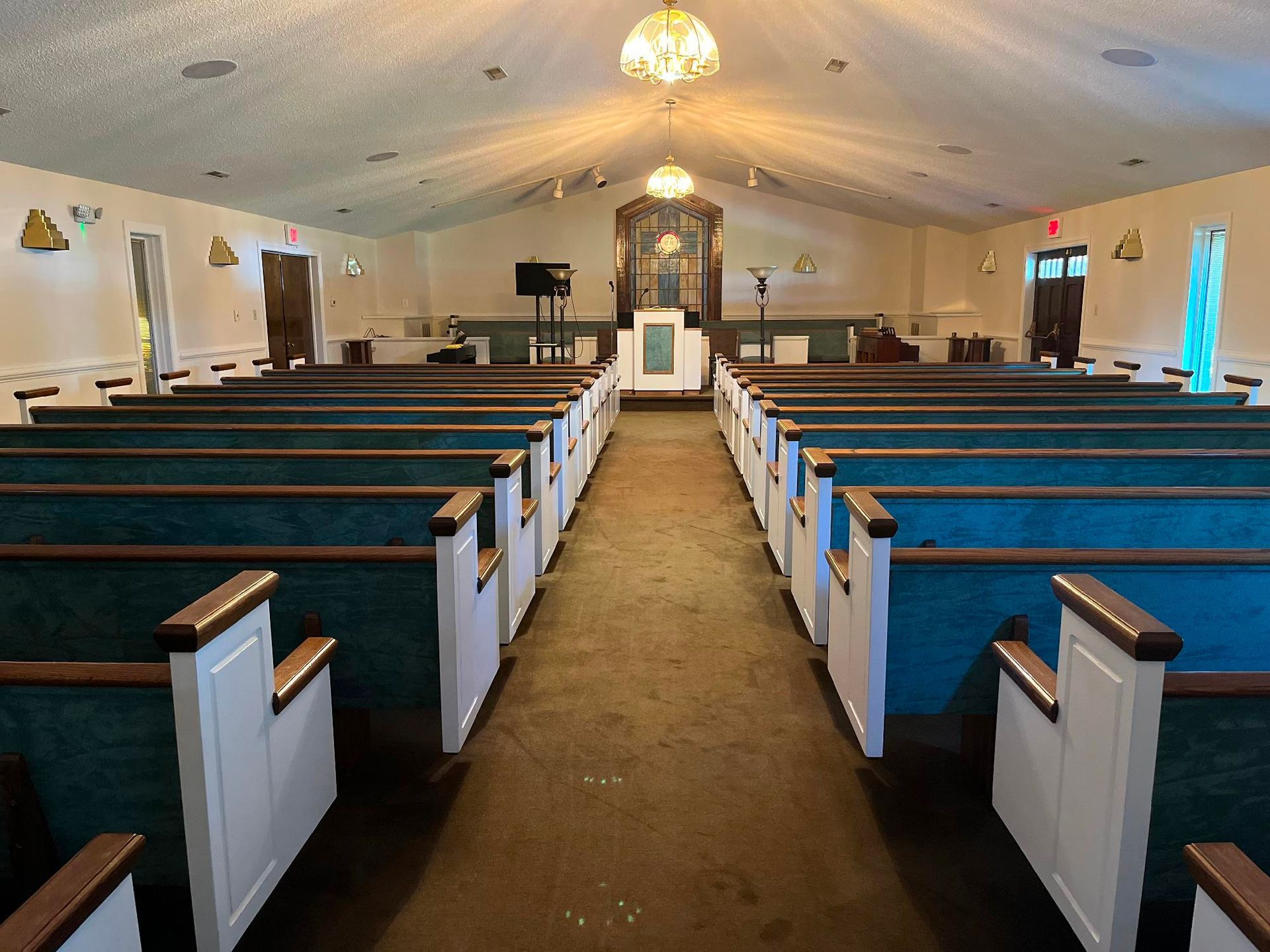 An empty church interior with rows of blue-cushioned wooden pews facing a central altar under a vaulted ceiling.