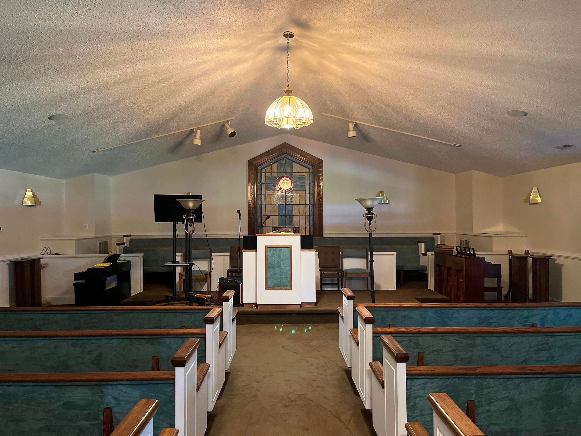 The interior of a church sanctuary with wooden pews, a central altar, and a large decorative window at the front.