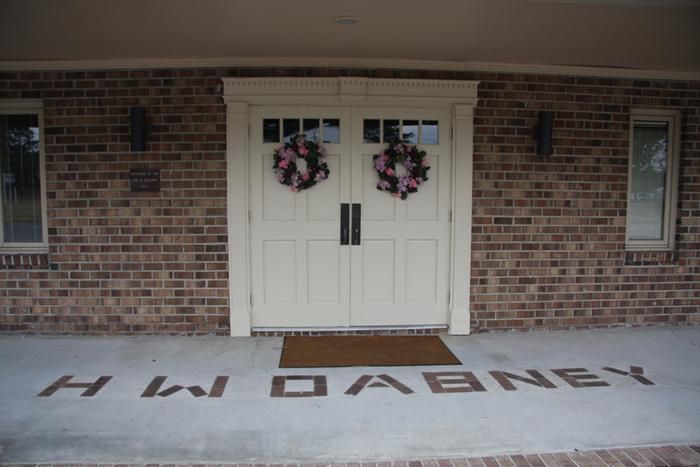 A brick building entrance with double white doors, floral wreaths, and the name 