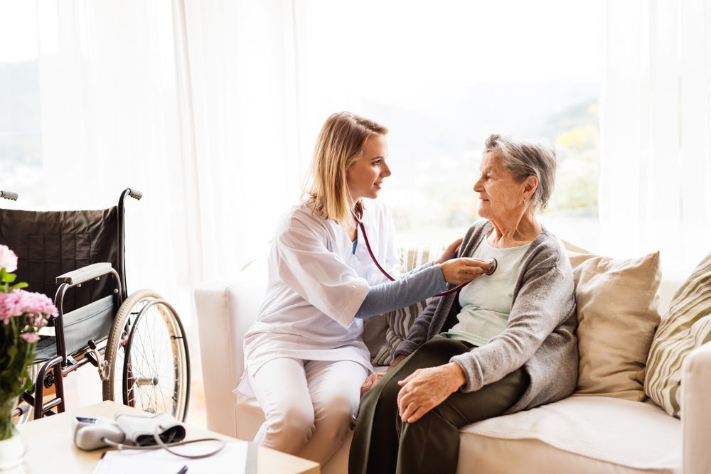 Caregiver Checking an Older Woman’s Pulse on A Sofa — Home Nursing Services in Liverpool, NSW
