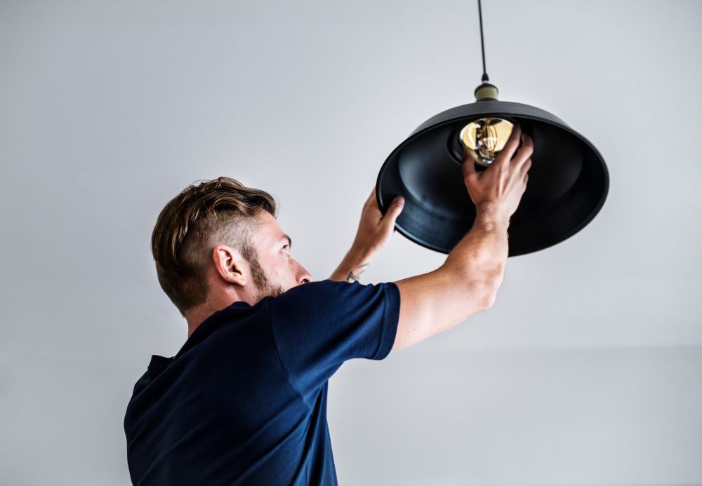 A Man is Installing a Light Fixture on a Ceiling — Home Nursing Services in Port Macquarie, NSW