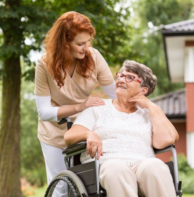 An Elderly Woman in A Wheelchair Is Being Helped by A Nurse — Home Nursing Services in Port Macquarie, NSW